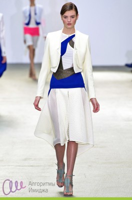 Модель демонстрирует ассиметричный наряд юбки, джемпера и жакета в контрастных цветовых сочетаниях молочного с синим и черным